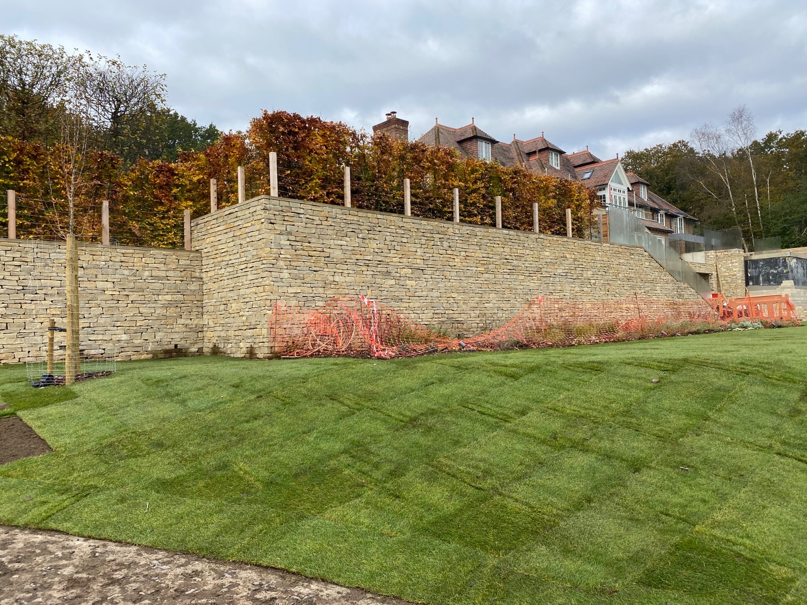 Large stone retaining wall with wooden posts and newly laid lawn